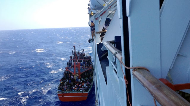 Kleines Boot, daneben Schiff. Leute im Boot.