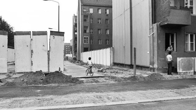 schwarzweiss Foto einer Strasse, dahinter Blöcke, links Mauerstücke.