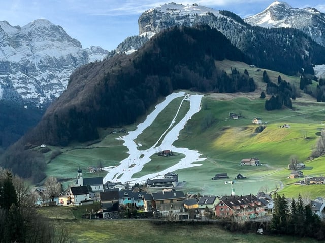 Blick auf grüne Landschaft und Kunschnee-Skipiste, die heraussticht