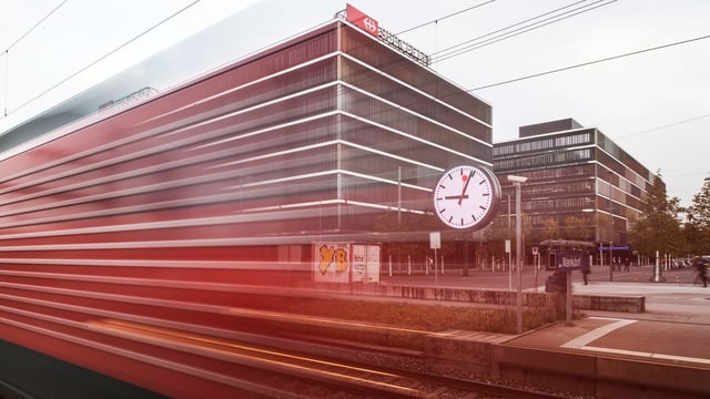 Ein Zug verschwimmt im Bild, hinten ist eine SBB-Uhr zu sehen.