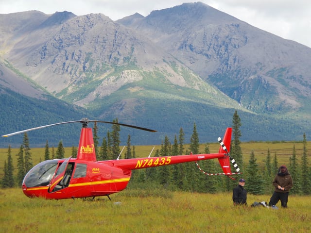 Ein roter Helikopter mit offener Türe auf dem Boden und zwei Menschen daneben.