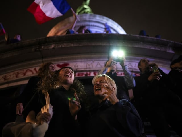 Menschen feiern mit Fahnen und Lichtern auf einem Denkmal bei Nacht.