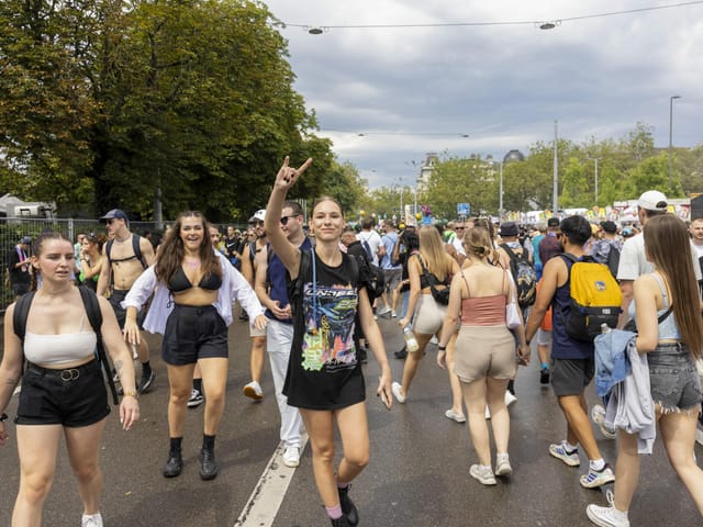 Viele Leute laufen auf einer Strasse. Ein Frau schaut in die Kamera, lacht und macht eine Geste.