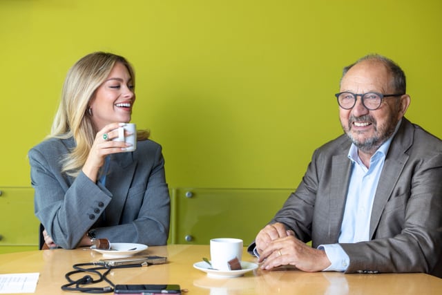 Jennifer Bosshard und Bernard Thurnheer sitzen am Tisch und lachen.