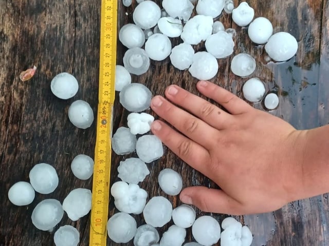 Hand neben Hagelkörnern und Lineal auf Holz.