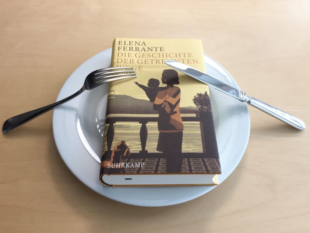 Band 3 Die Geschichte der getrennten Wege von Elena Ferrante liegt auf einem weissen Teller. Messer und Gabel signalisieren, dass Annette König davon nicht genug kriegt.