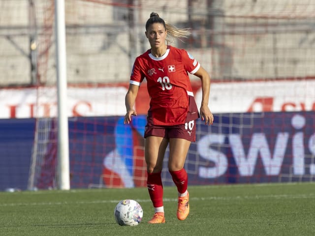 Fussballspielerin im roten Trikot mit dem Ball auf dem Spielfeld.