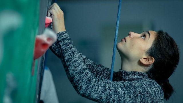 Grossaufnahme Frau, die Kletterwand hinaufschaut.