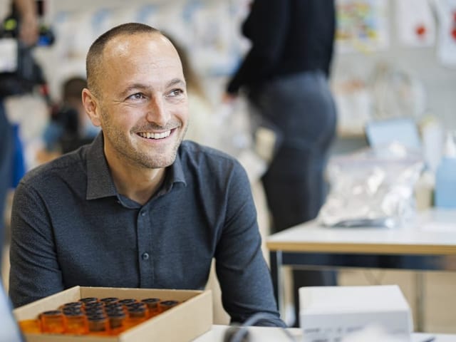 Ein Mann mit kurzgeschorenem Haar sitzt in einem Schulzimmer. 