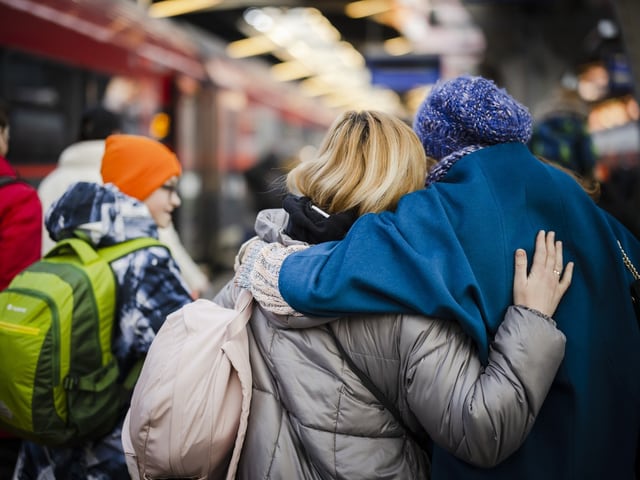 Personen umarmen sich auf einem Bahnhof.