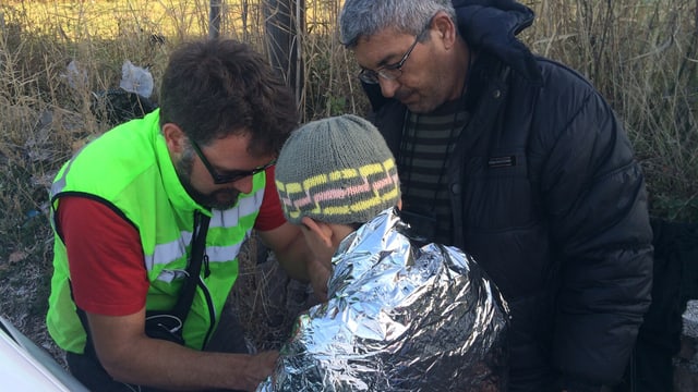 Ein Mann kleidet einen Jungen mit einer Rettungsdecke ein 