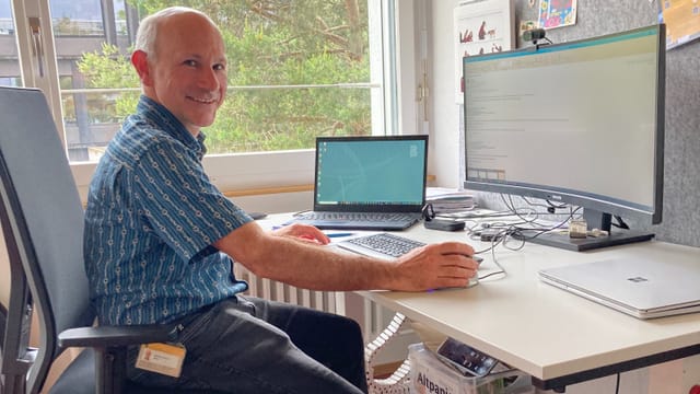 Mann sitzt an Schreibtisch mit Computer und Monitor im Büro.