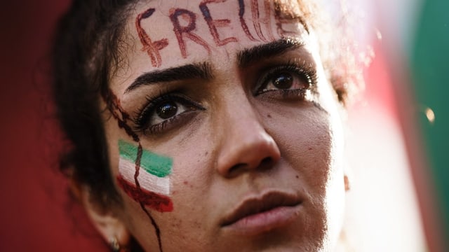 Frau mit Iran-Flagge auf der Wange und «Freiheit» auf der Stirn geschrieben.