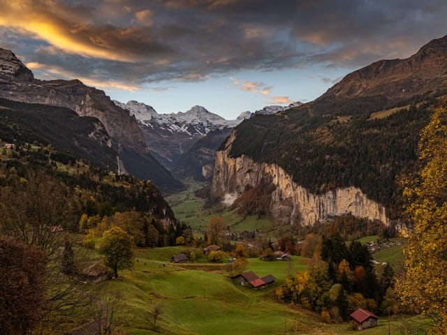 Herbstliche Berglandschaft mit Tal, Hütten und Wolkenhimmel.