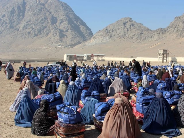 Afghanische Familien sitzen mit dem Rücken zur Kamera auf einem sandigen Boden in der Wüste.