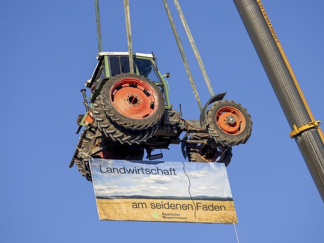 Ein Traktor wird mit einem Banner an einem Kran hochgezogen.