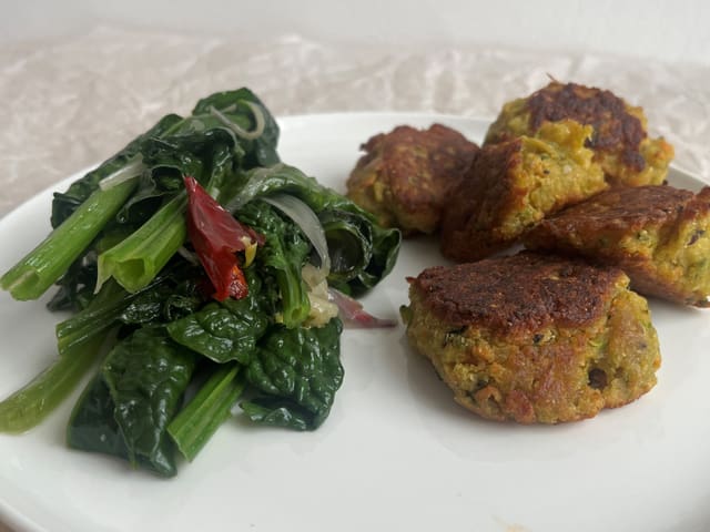 Kleine  Pakoras-Bällchen aus diversen Gemüsen und Kichererbsenmehl  und Spinat auf einem weissen Teller.