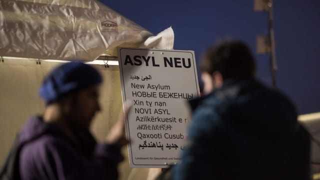 Zwei Flüchtlinge vor einer Tafel mit der Aufschrift «Asyl Neu»