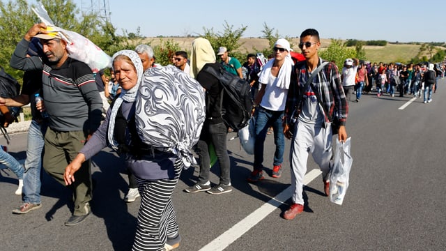 Menschen mit Sack und Pack marschieren auf einer Landstrasse.