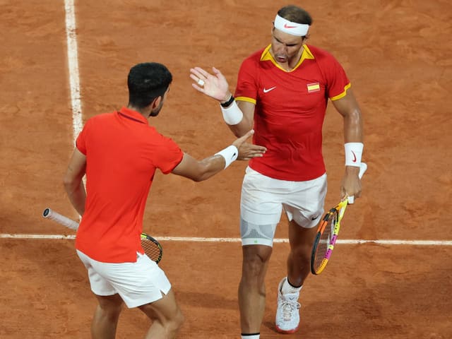 Zwei Tennisspieler in roten Hemden beim Spielen auf Sandplatz.