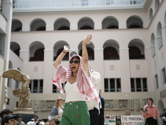 Ein Mensch mit erhobenen Armen bei einer Versammlung in einem Innenhof.