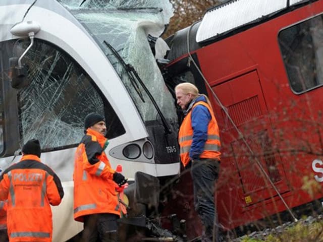 Ermittler stehen vor der Unfallstelle. Im Hintergrung ein zerstörter Triebwagen.