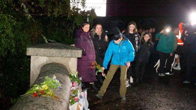 Menschen legen Blumen auf Mauer nieder.