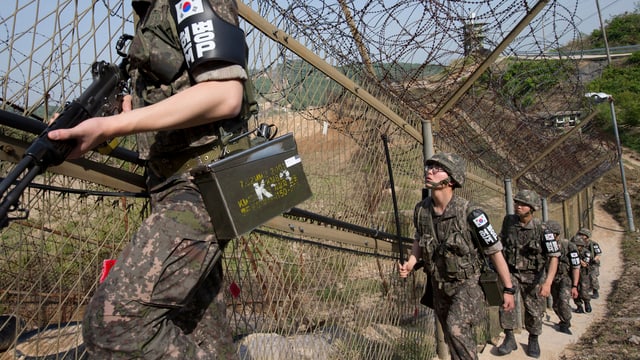 Soldaten laufen einen Stacheldrahtzaun entlang.