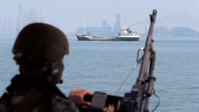 Symbolbild: Ein Soldat mit Helm und Gewehr schaut aufs Meer und einen Öltanker.