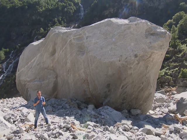 Mann vor riesigem Felsen im Gebirge.