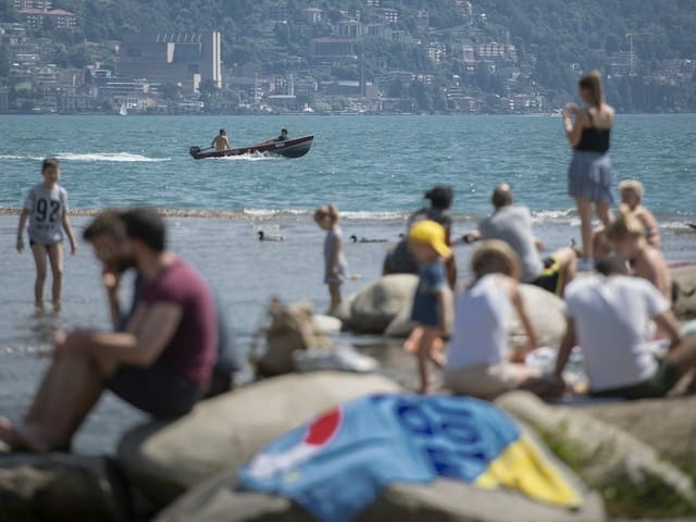 Menschen am See, darauf ein Fischerboot.