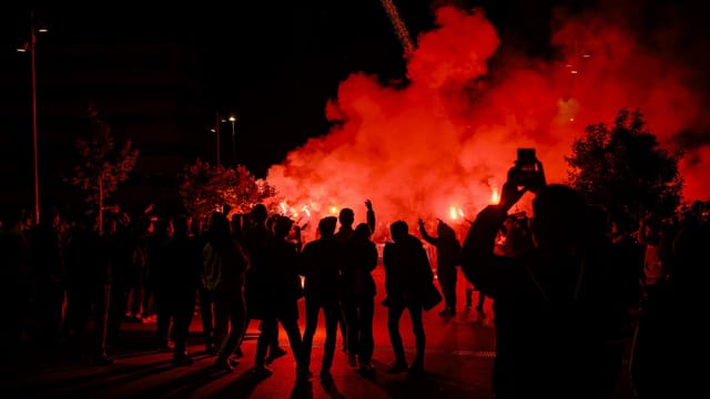 Menschen stehen im Vordergrund, im Hintergrund sind eine grosse, rote Wolke und brennende Feuerwerkskörper zu sehen