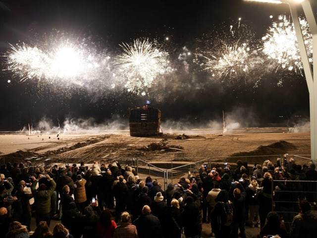 Menschen beobachten Feuerwerk über einem Strand.