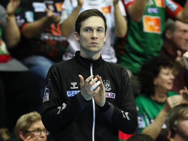 Junge Person mit schwarzer Jacke klatscht in einer Sporthalle.