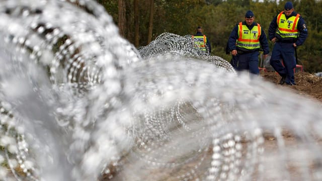 Ungarische Grenzwächter stehen hinter Rollen von Stacheldraht.