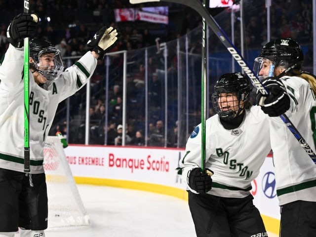 Drei Eishockeyspielerinnen von Boston in voller Ausrüstung feiern ein Tor auf dem Eis.