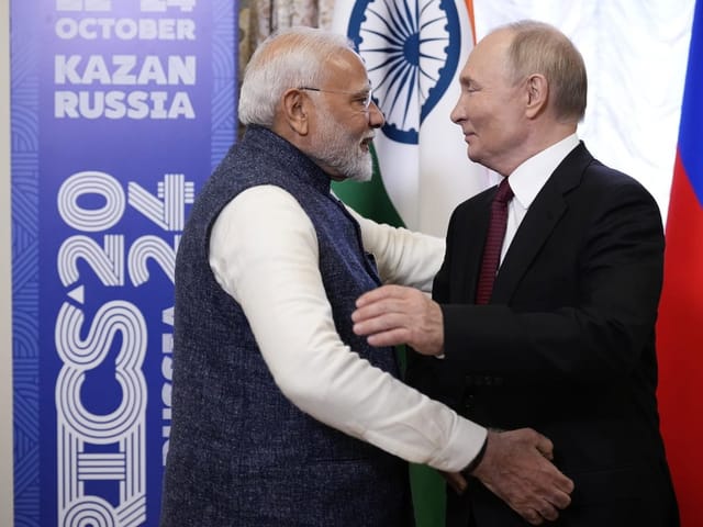 Modi und Putin schütteln sich die Hand vor Flaggen.