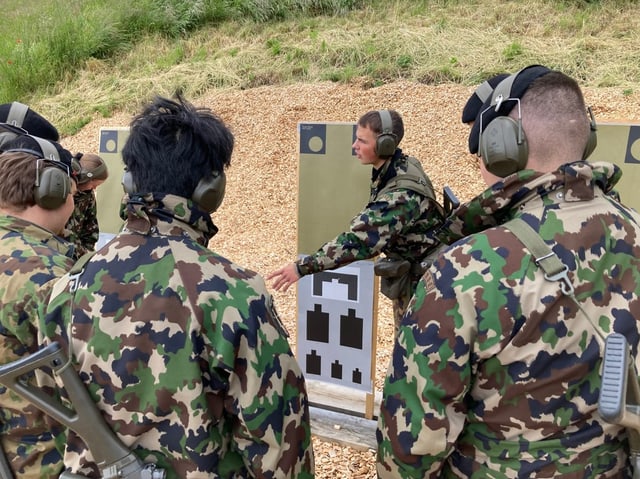 Soldaten in Tarnuniform hören auf dem Schiessstand den Anweisungen eines Ausbilders zu.