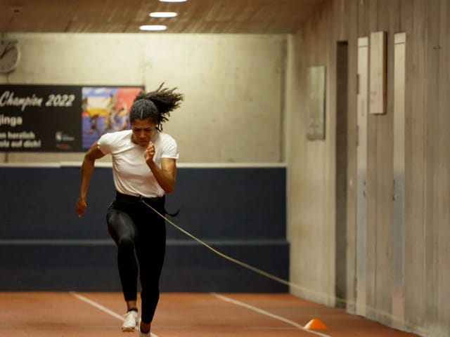 Frau rennt auf einer Laufbahn in einer Sporthalle.