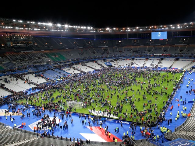 Hunderte Leute stehen auf dem grünen Spielfeld des Stadions. Die Ränge sind praktisch leer. 