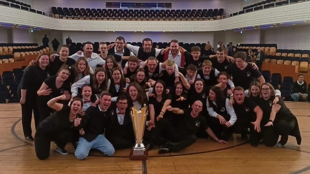 Die Brass Band 13 Étoiles Formation B vor einem grossen Siegerpokal.