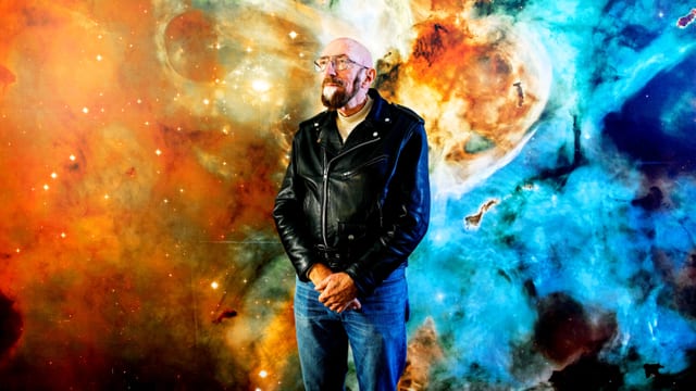 Kip Thorne vor einer Wand mit Kosmos-Muster.