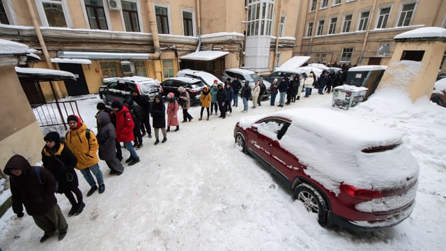 Eine lange Schlange Menschen steht in der Kälte an. Es liegt viel Schnee