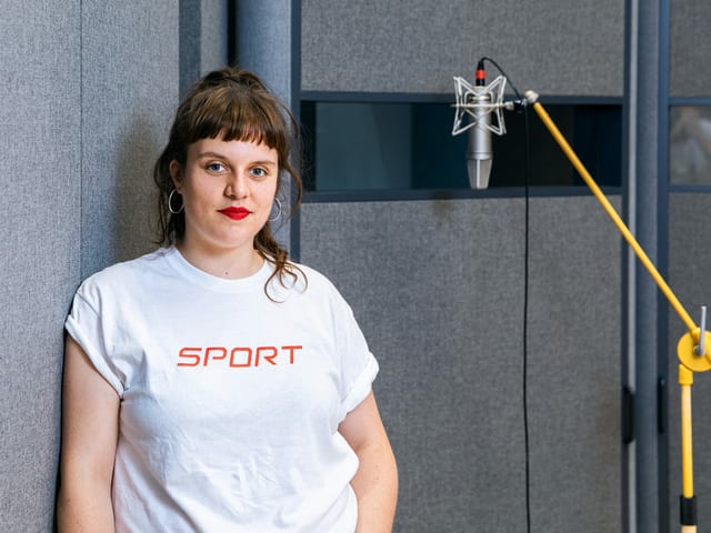 Frau in weisem T-Shirt vor einer grauen Wand.