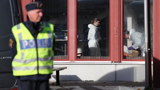 Ein schwedischer Polizist steht vor der Schule, darin untersuchen Spezialisten in weissen Overalls den Tatort.