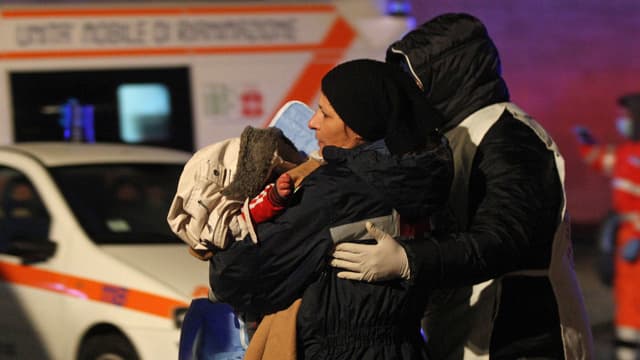 Eine Frau mit einem Baby im Arm wird von einem Helfer zu einer Ambulanz begleitet.