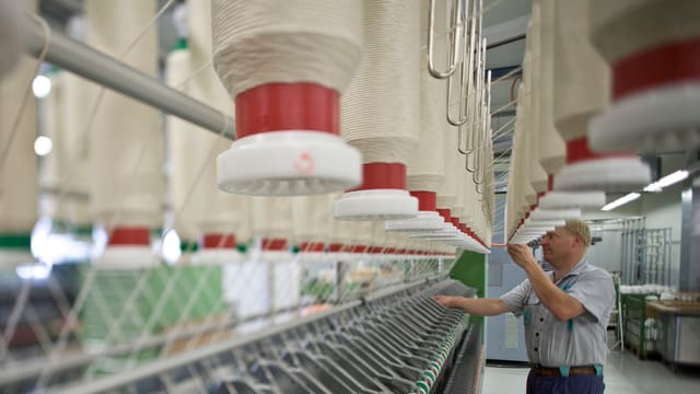 Ein Arbeiter kontrolliert die Spindeln einer Spinnereimaschine