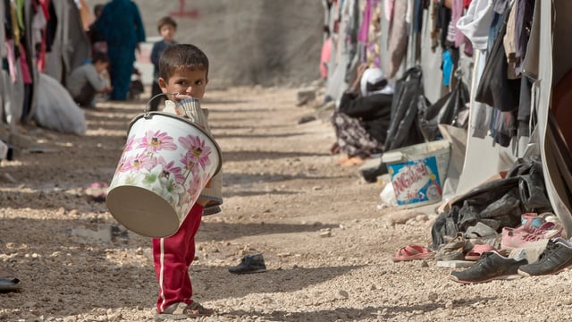 Kleines Flüchtlingskind mit Wassereimer in einem Lager an der türkisch-syrischen Grenze