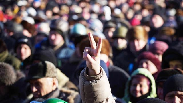 Eine Menschenmenge in der Ukraine, der Fokus liegt dabei auf einen ausgestreckten Arm, dessen Finger ein Victory-Zeichen bilden. 