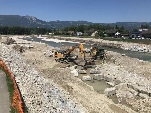 Bagger und Lastwagen auf Kiesbank im Fluss.